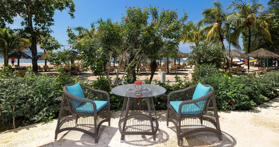 Beachfront patio seating for a villa suite at Sandals Negril with table, chairs and garden view.