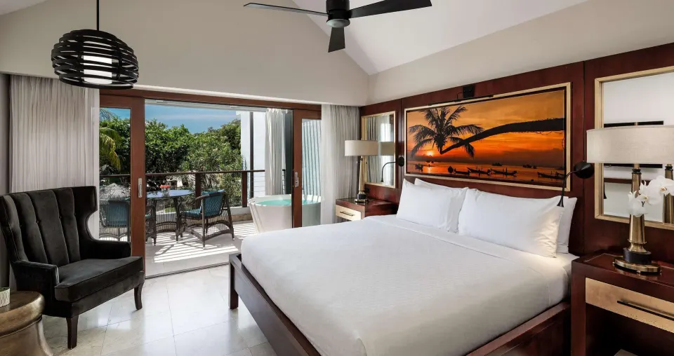 King bedroom in a beachfront villa suite at Sandals Negril with balcony and soaking tub visible.