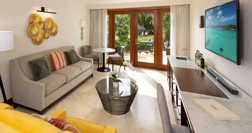 Living room in a beachfront villa suite at Sandals Negril with sofa, TV, wet bar and patio doors.