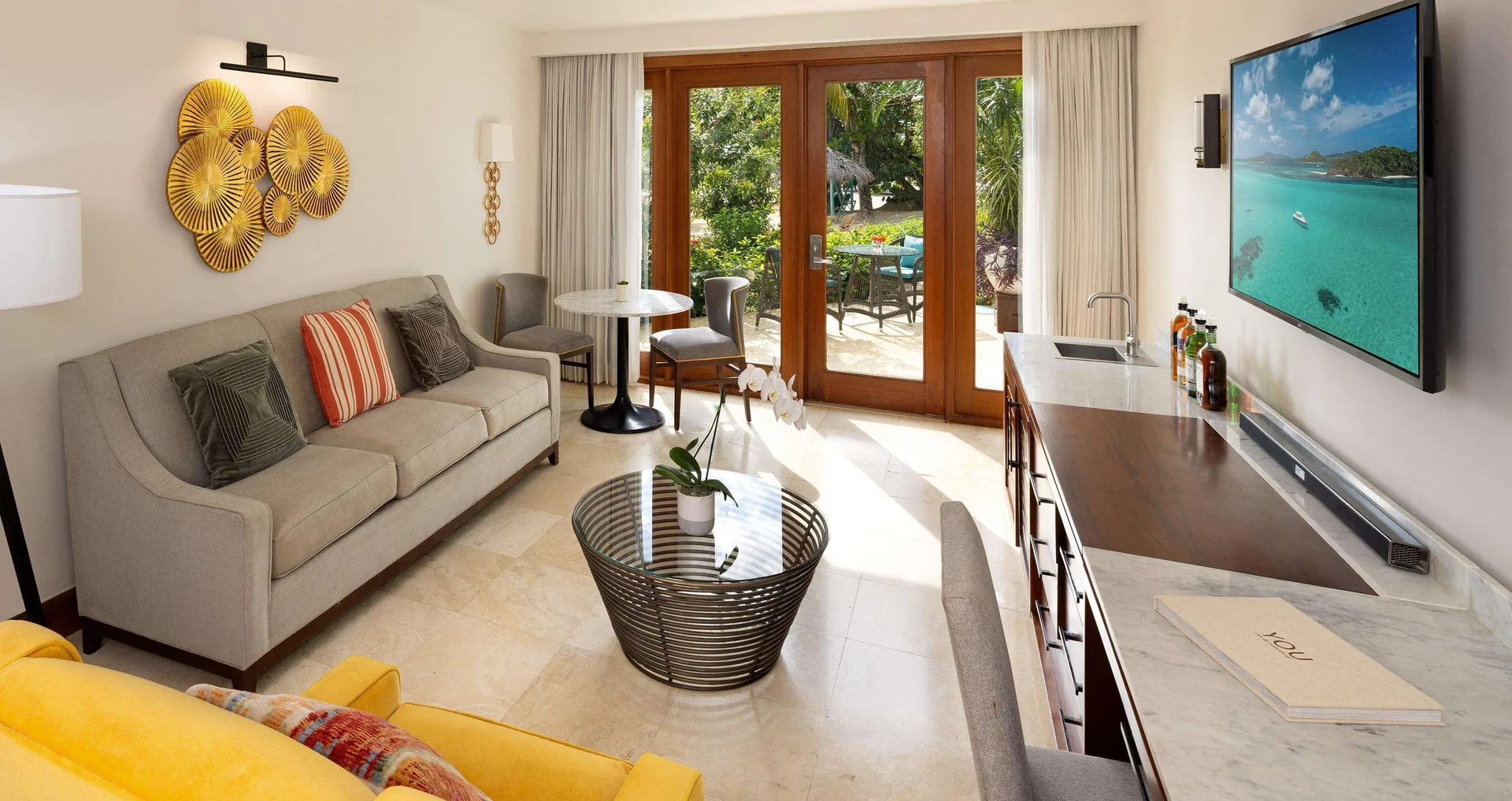 Living room in a beachfront villa suite at Sandals Negril with sofa, TV, wet bar and patio doors.