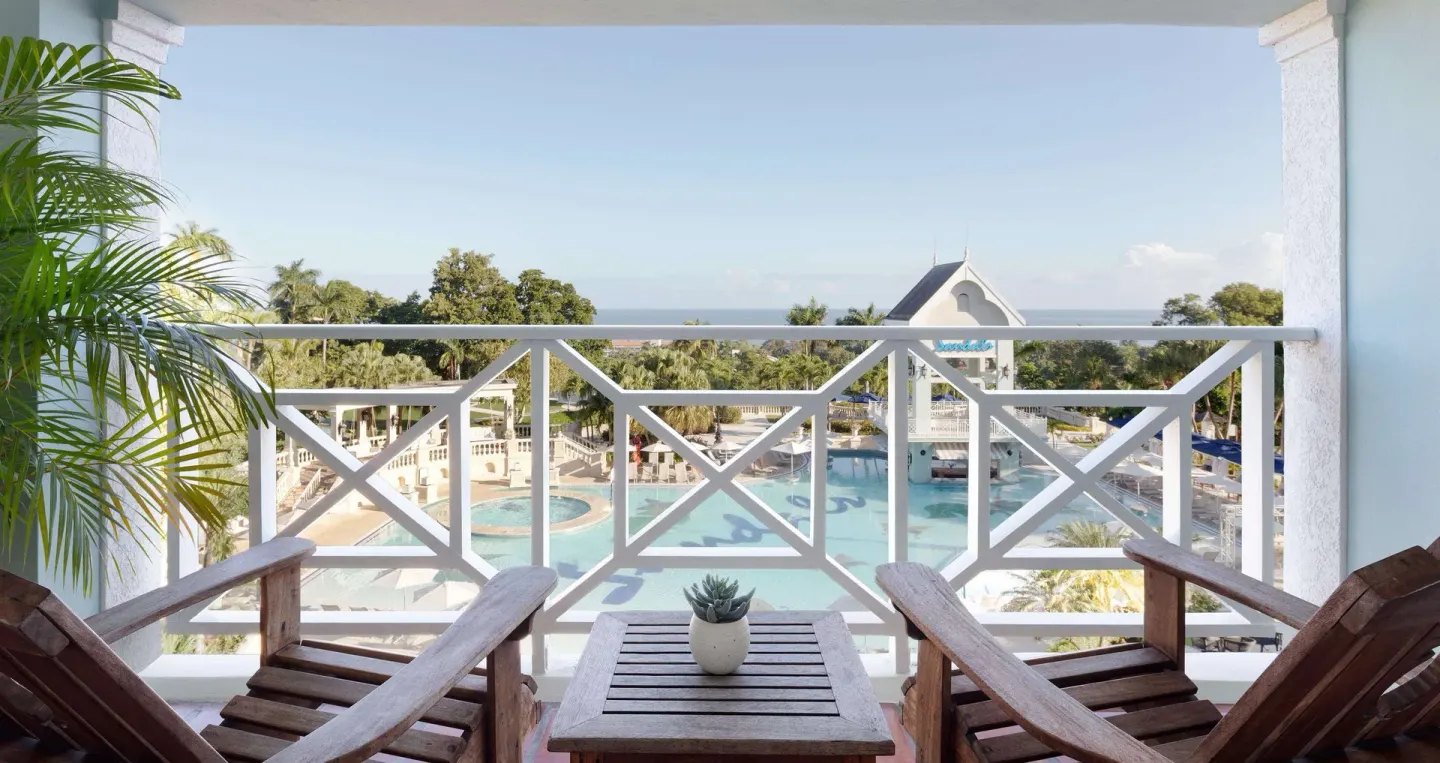 Balcony with wooden chairs overlooking the main pool and ocean at Sandals Ochi.