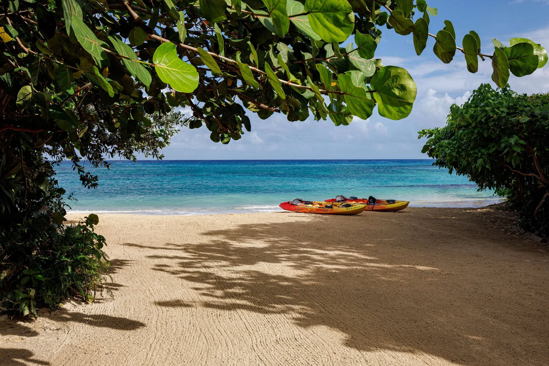 Sandy beach framed by leafy trees with kayaks by the water at Sandals Ochi.