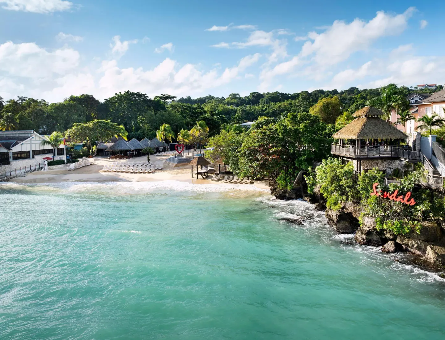 Aerial view of the beach, turquoise water, and thatched overlook at Sandals Ochi.