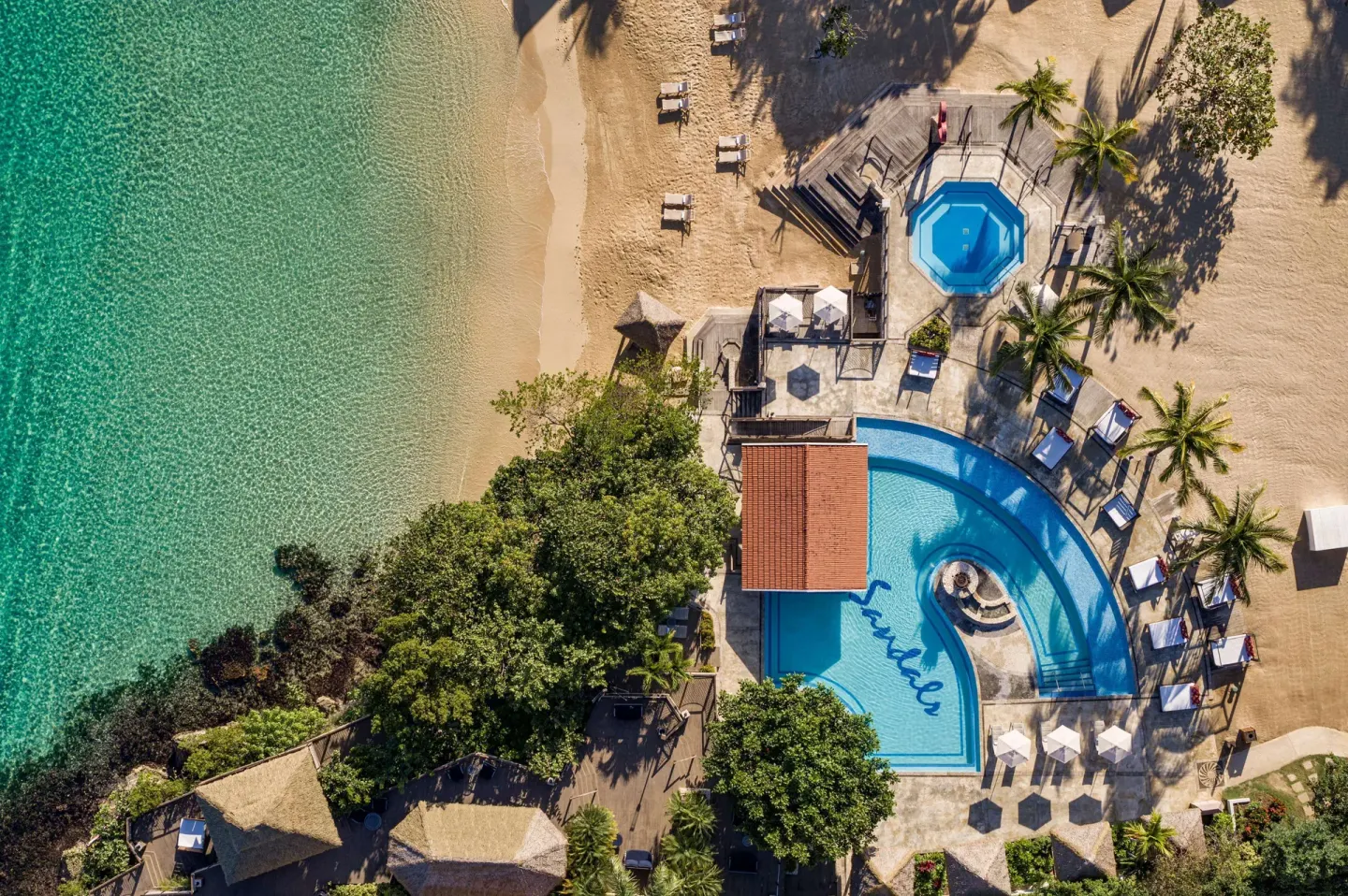 Aerial view of beachside pools, palm trees, and clear water at Sandals Ochi.