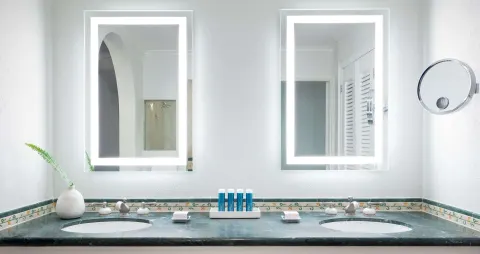 Double vanity bathroom with lit mirrors and blue bath amenities at Sandals Ochi.