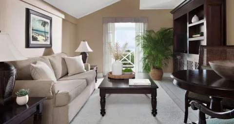Guest room sitting area with sofa, coffee table, and balcony doors at Sandals Ochi.