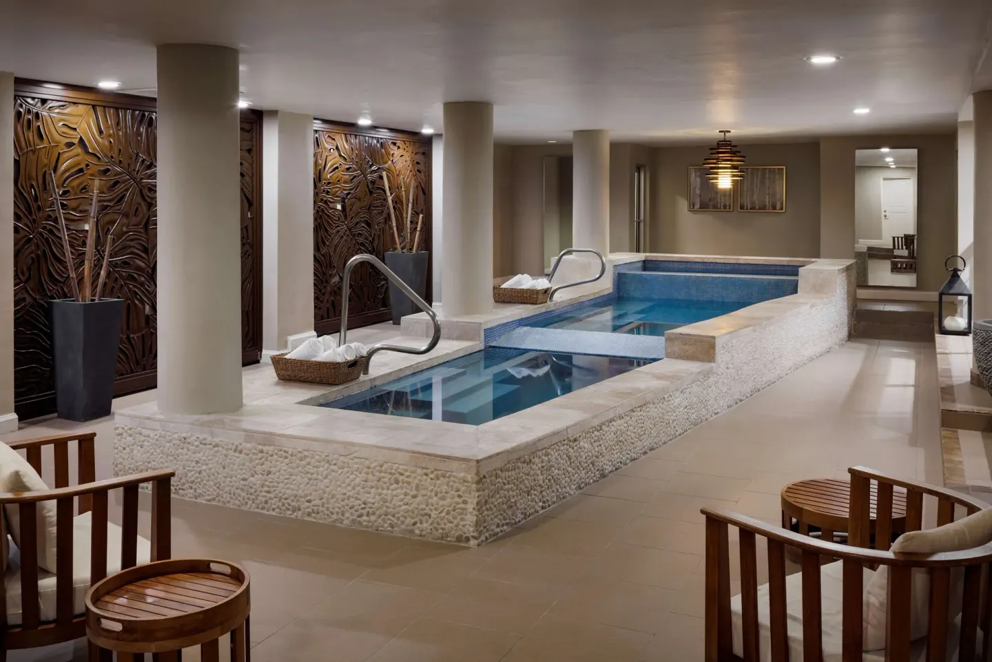 An indoor spa plunge pool with seating and carved wall panels is shown at Sandals Ochi.
