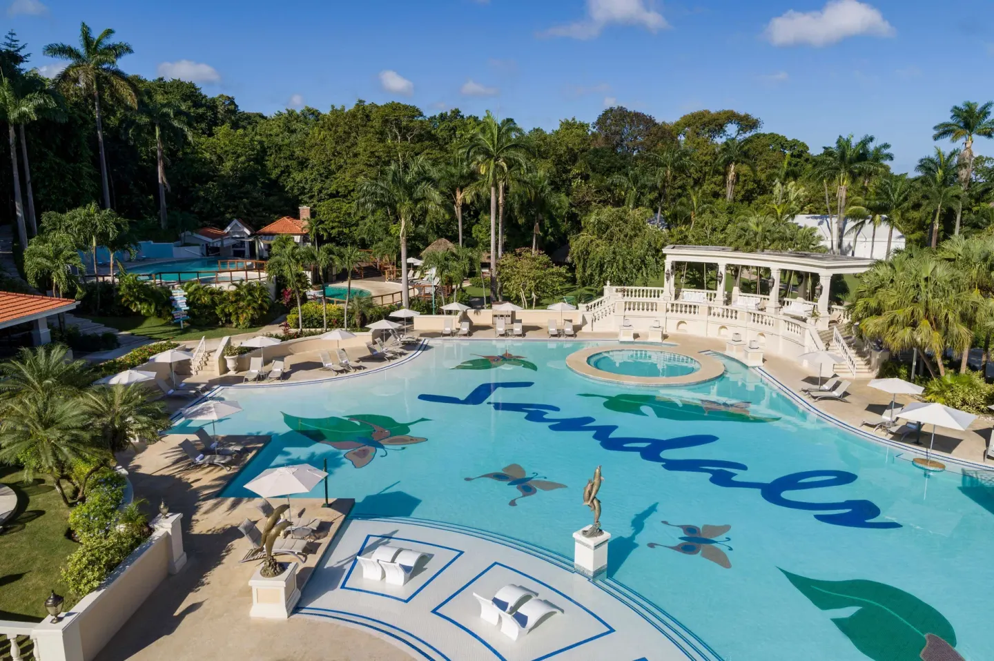 Aerial view of the main pool with loungers, umbrellas, and palms at Sandals Ochi.