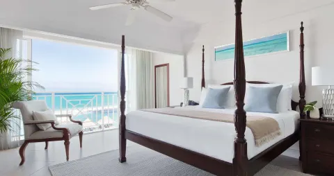 Guest room with four-poster king bed and ocean-view balcony at Sandals Ochi.
