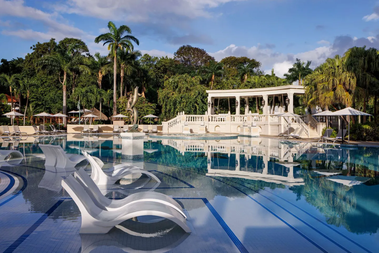 Shallow pool loungers, a statue, and a white colonnade by the water at Sandals Ochi.