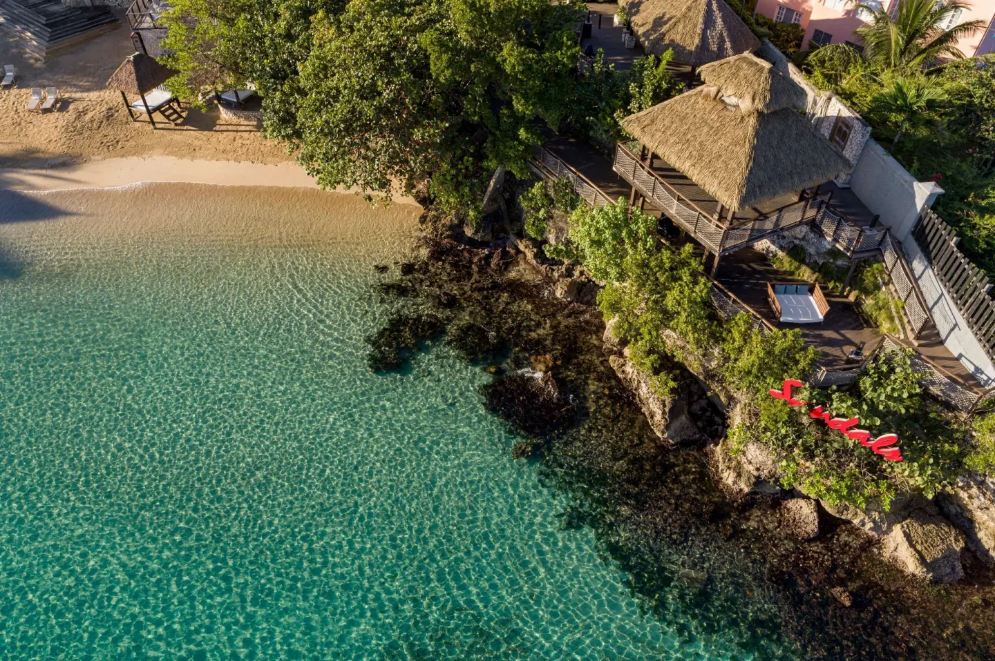 Aerial view of rocky shoreline, clear water, and thatched deck at Sandals Ochi.