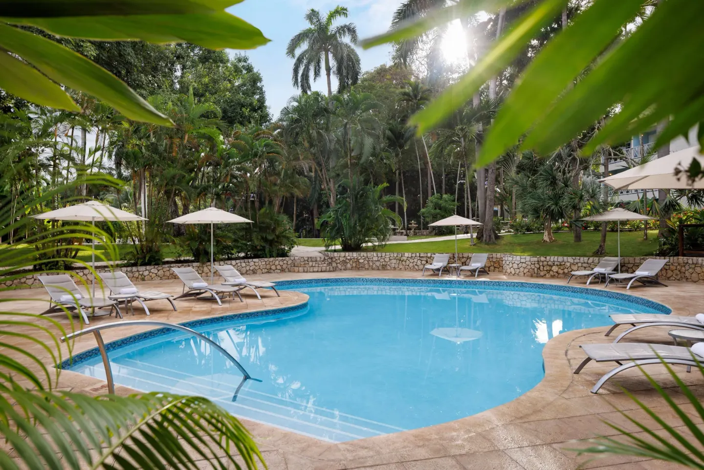 A curving garden pool with loungers and umbrellas sits among palms at Sandals Ochi.