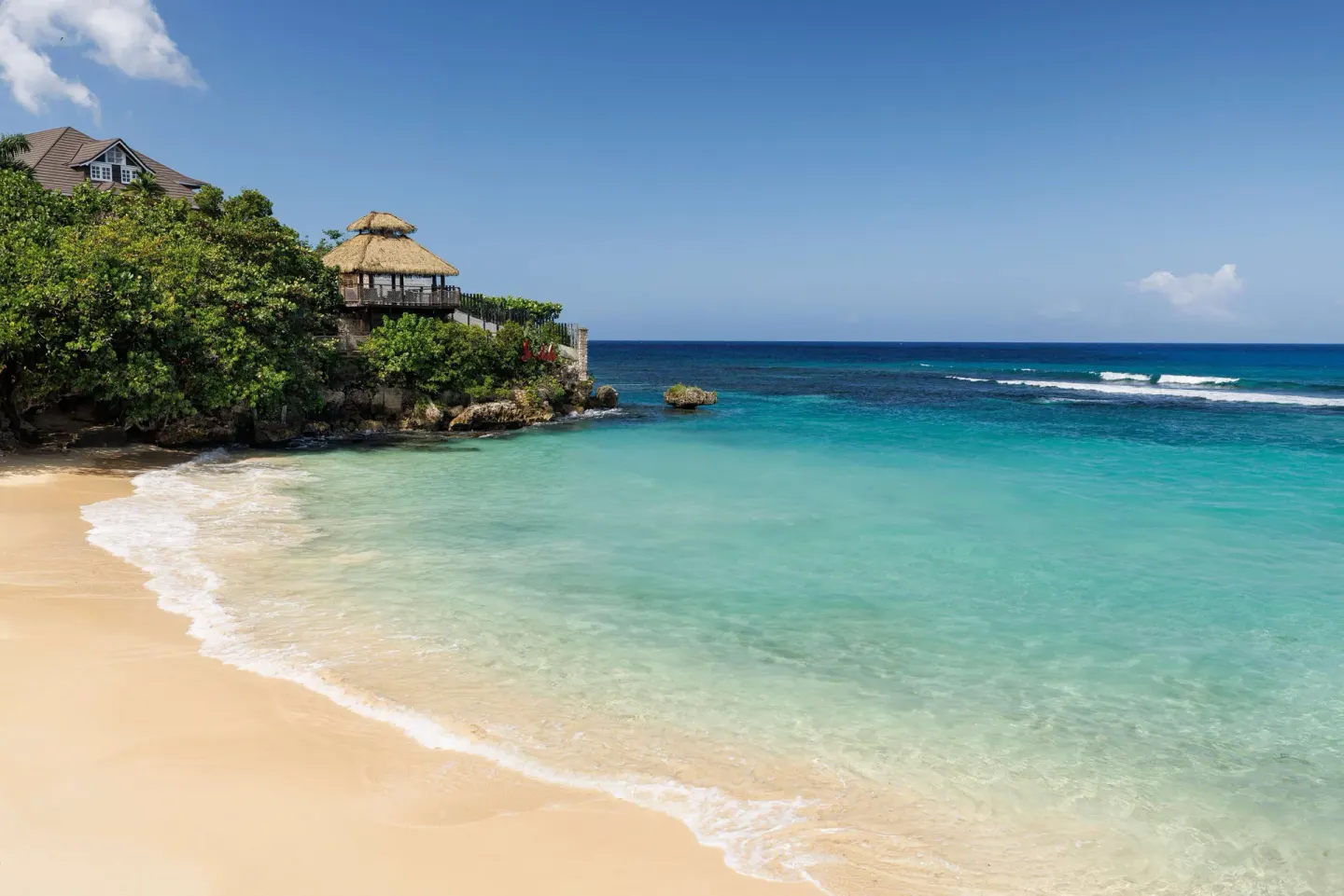 Clear turquoise water and sandy cove with a thatched lookout at Sandals Ochi.