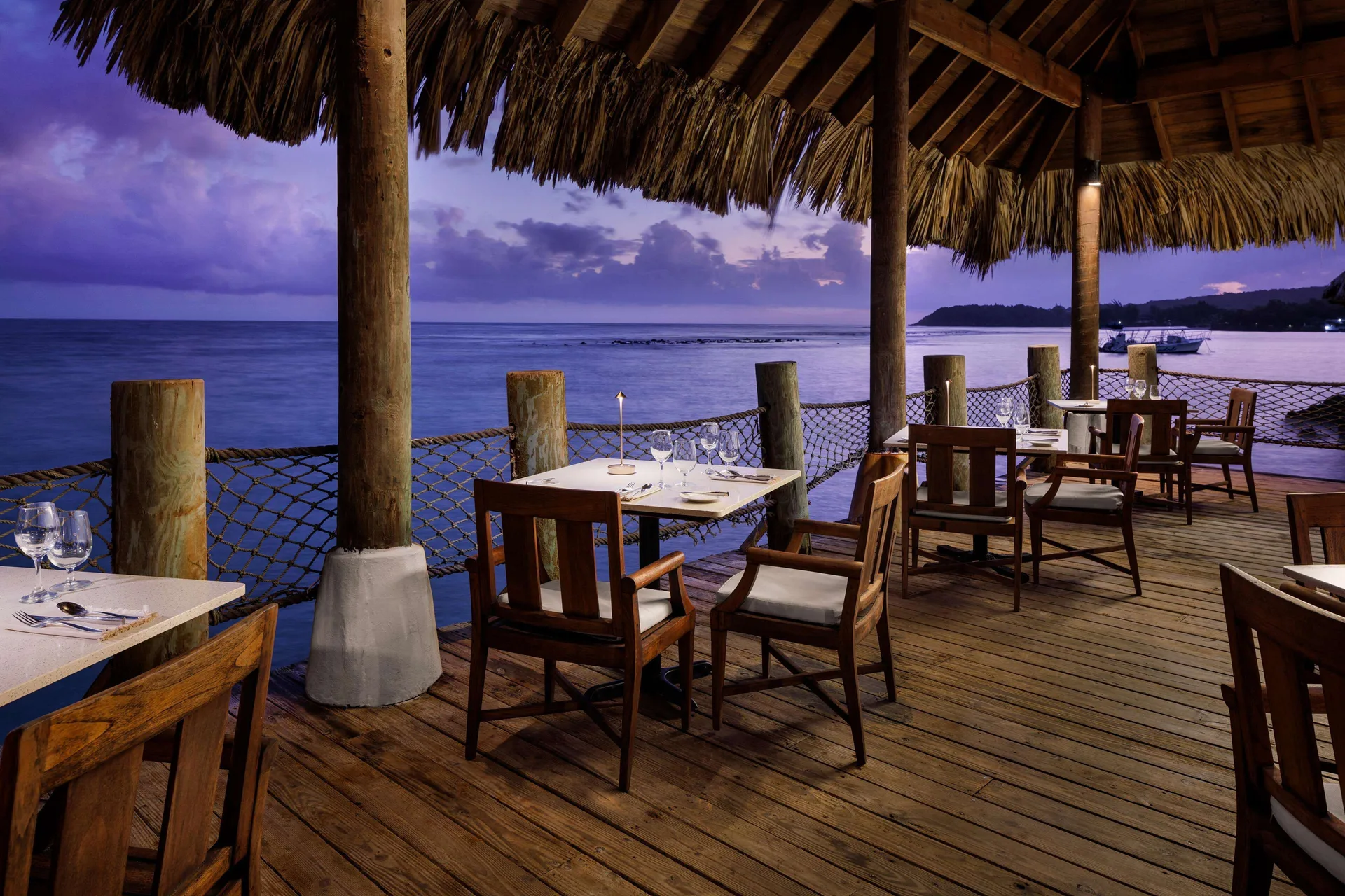 Overwater deck dining tables under a thatched roof at Sandals Ochi.