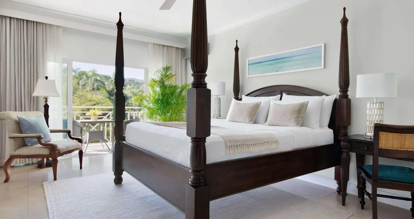 Four-poster king bed in a Luxury Room at Sandals Ochi with balcony doors and garden view beyond.