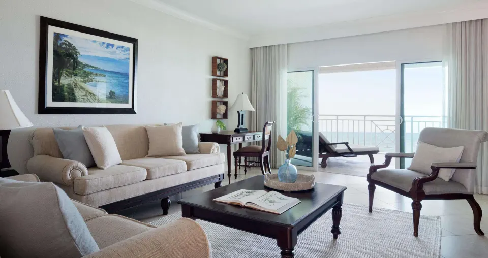 Separate sitting area in a Luxury Room at Sandals Ochi with sofa, armchairs, desk, and balcony doors.