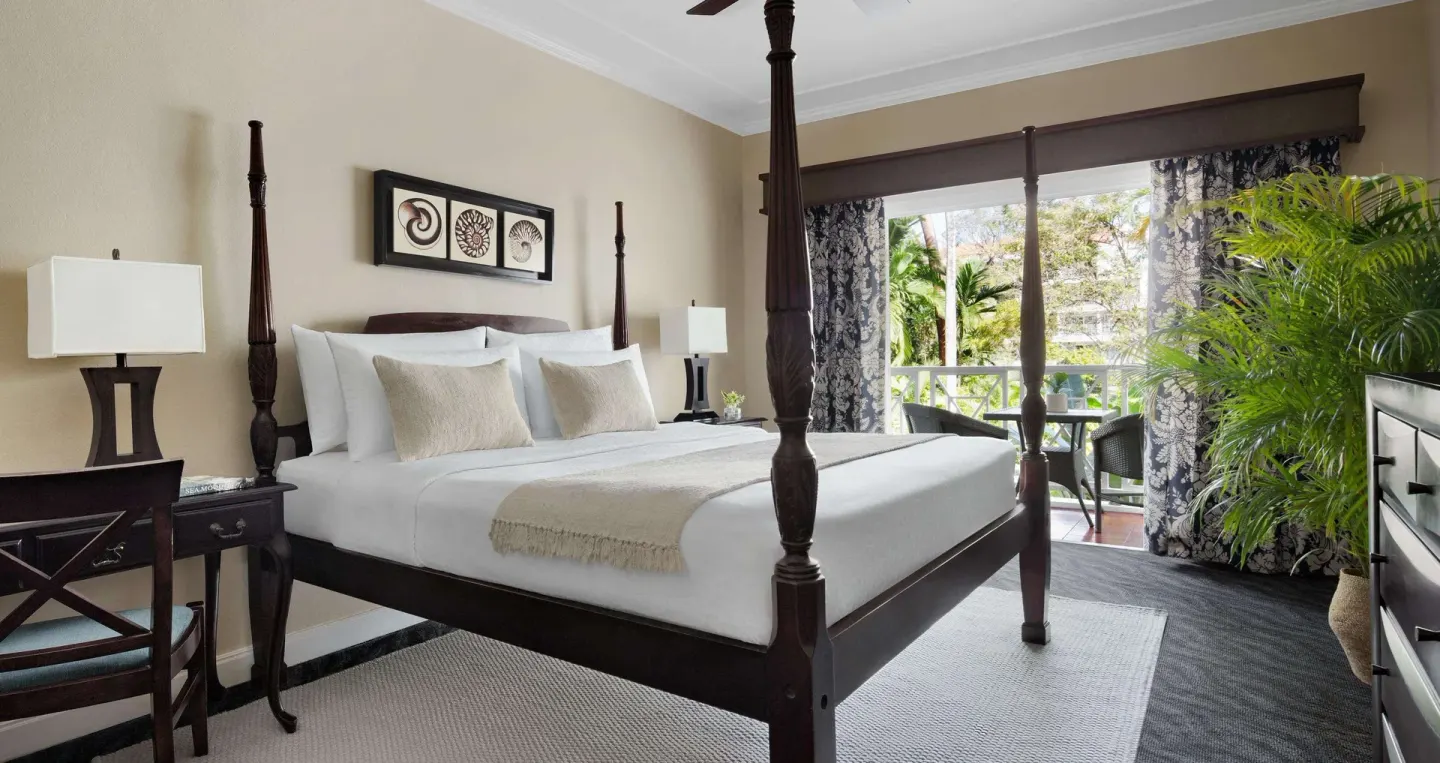 Four-poster king bed in a Premium Garden View room at Sandals Ochi with balcony doors open.