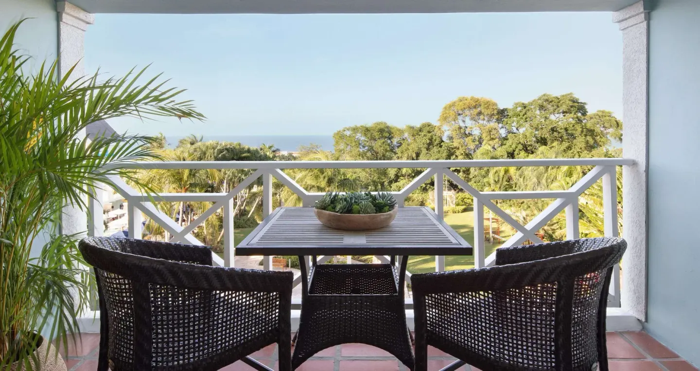 Furnished balcony with ocean and garden view from a Great House Oceanview room at Sandals Ochi.