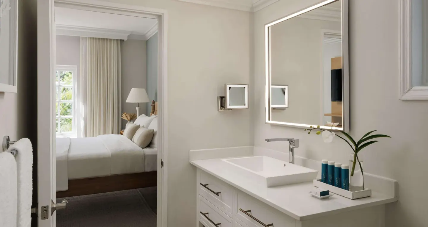 Bathroom vanity with illuminated mirror and bedroom beyond at Sandals Ochi.