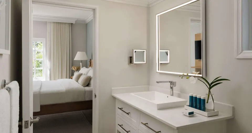 Bathroom vanity with illuminated mirror and bedroom beyond at Sandals Ochi.