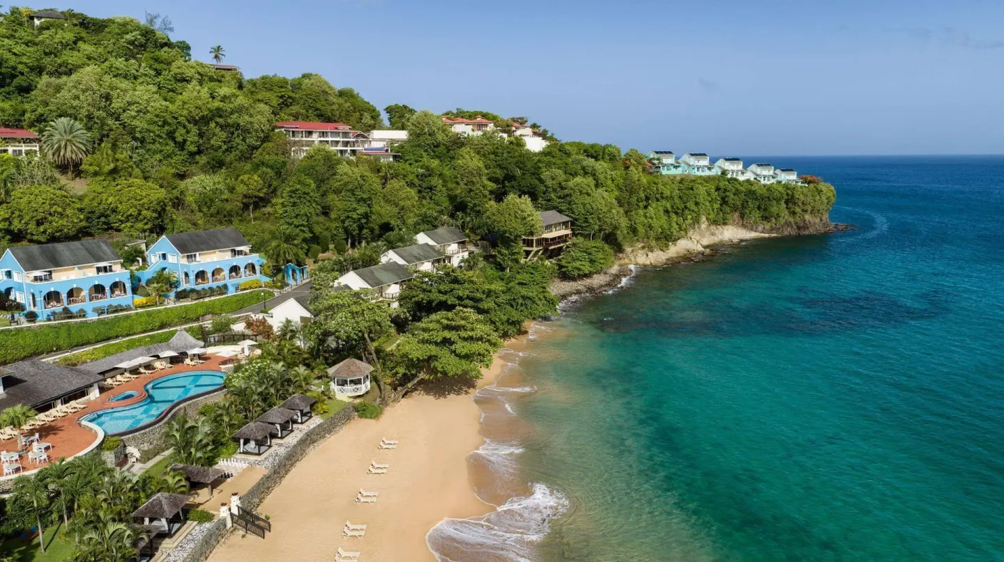 Aerial view of Sandals Regency La Toc with beach, pool, hillside rooms, and turquoise sea.