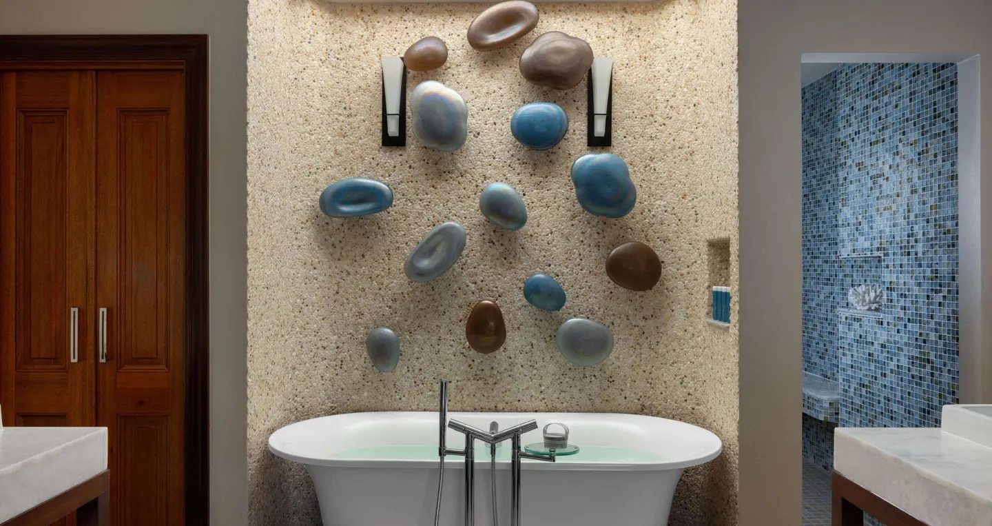 Bathroom soaking tub with pebble wall décor and blue-tile shower at Sandals Regency La Toc.