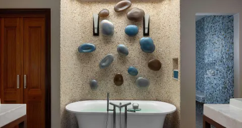 Bathroom soaking tub with pebble wall décor and blue-tile shower at Sandals Regency La Toc.