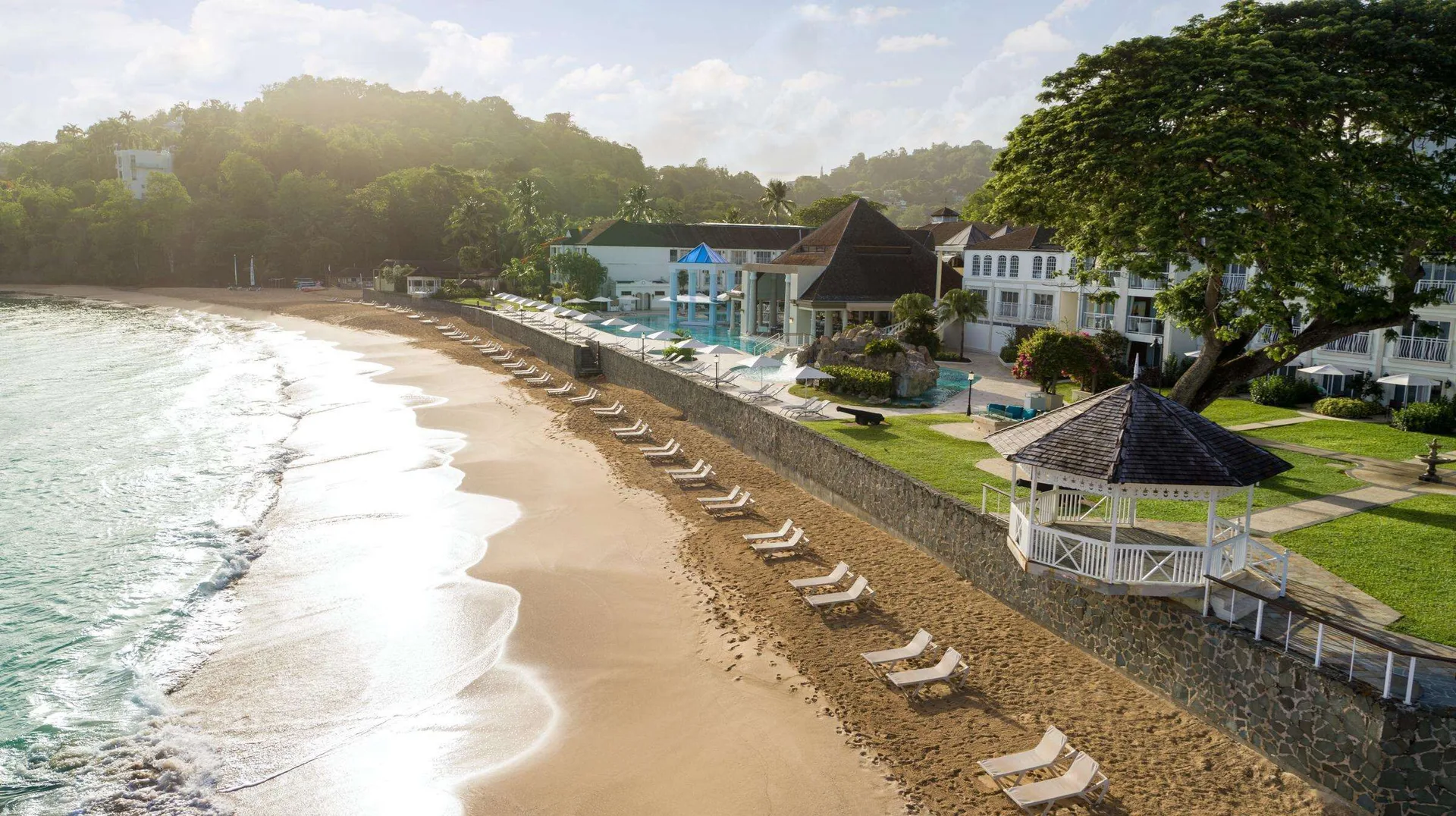 Beach loungers, gazebo, pool area, and beachfront buildings at Sandals Regency La Toc.