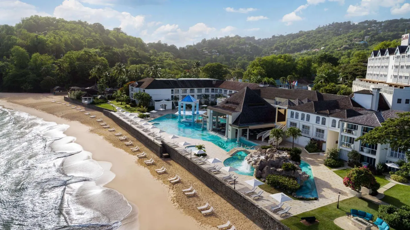 Beachfront resort buildings, pool deck, and sandy shore at Sandals Regency La Toc.