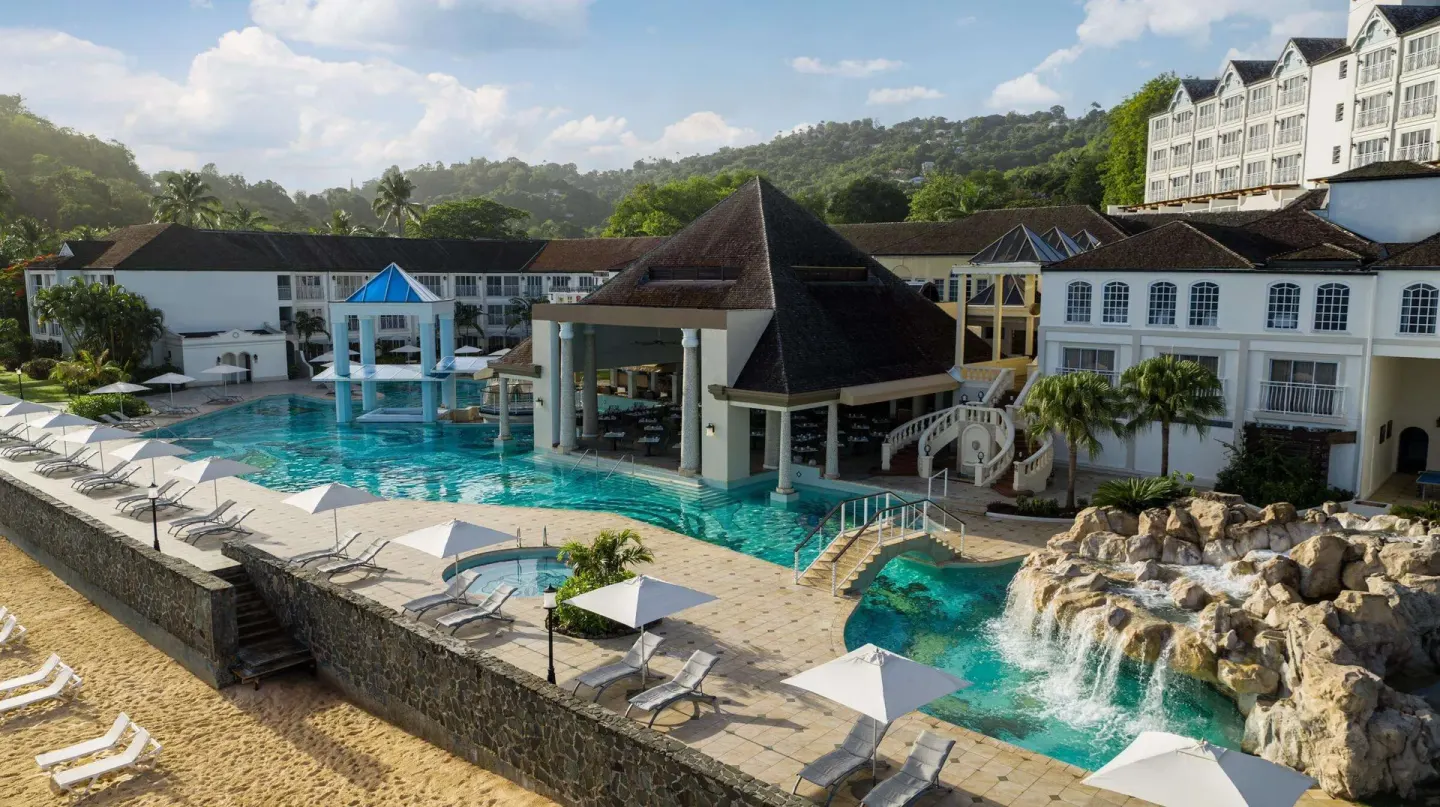 Main pool with waterfall rocks and beachfront loungers at Sandals Regency La Toc.