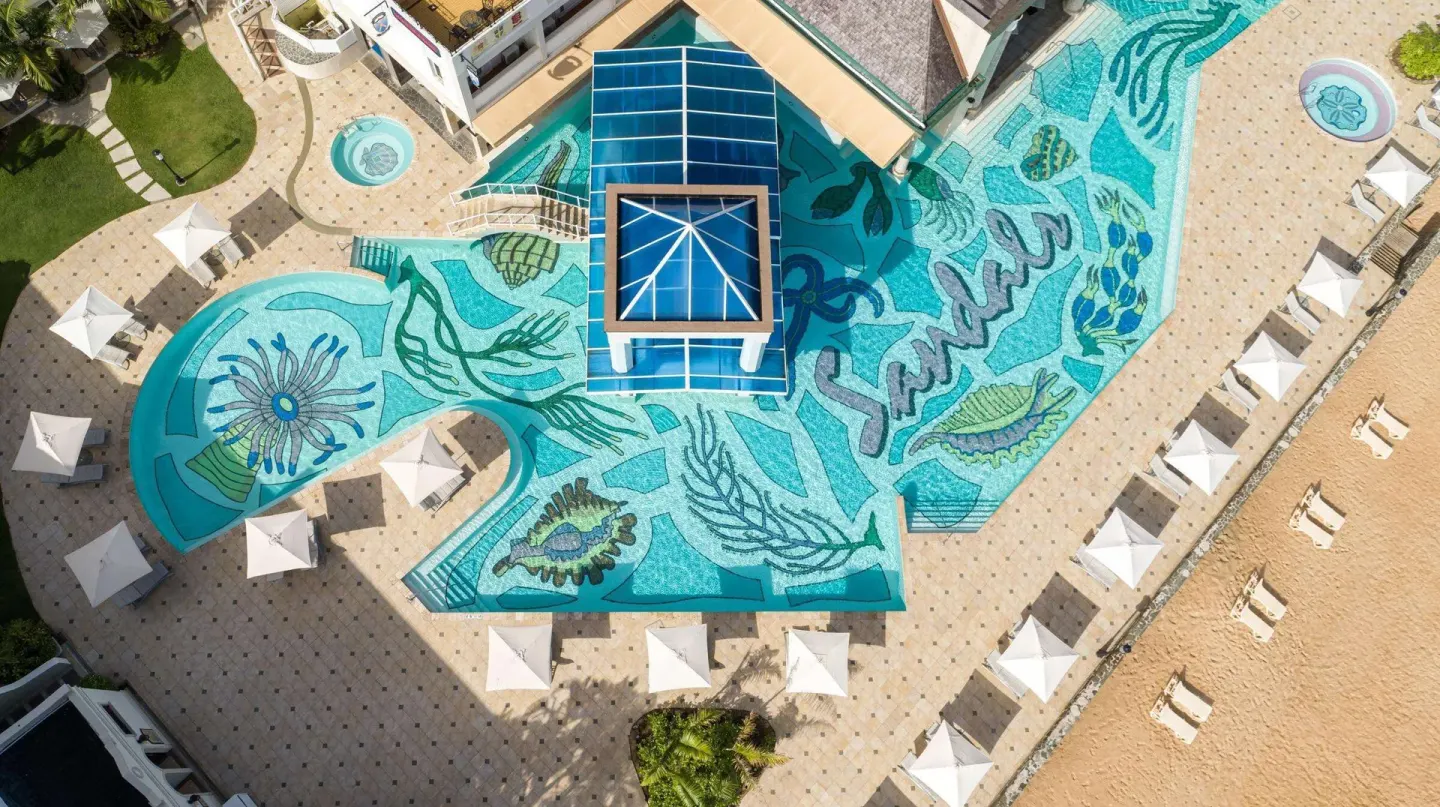 Overhead view of the mosaic pool deck and beach umbrellas at Sandals Regency La Toc.