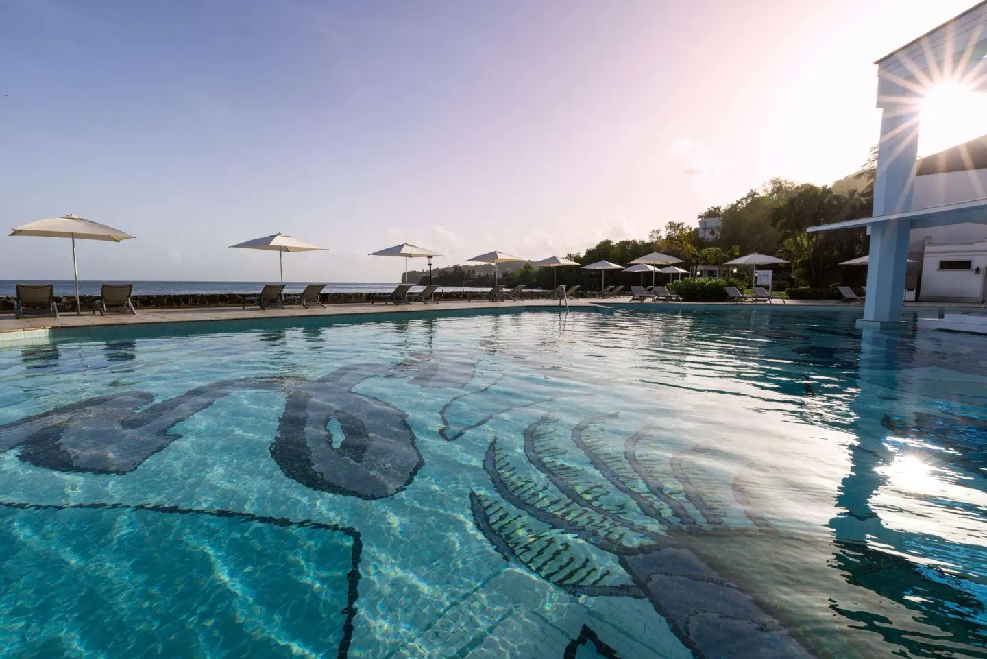 Low view across a mosaic pool with umbrellas and sea beyond at Sandals Regency La Toc.