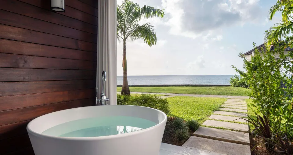 Outdoor soaking tub beside a garden path and ocean view at Sandals Regency La Toc.