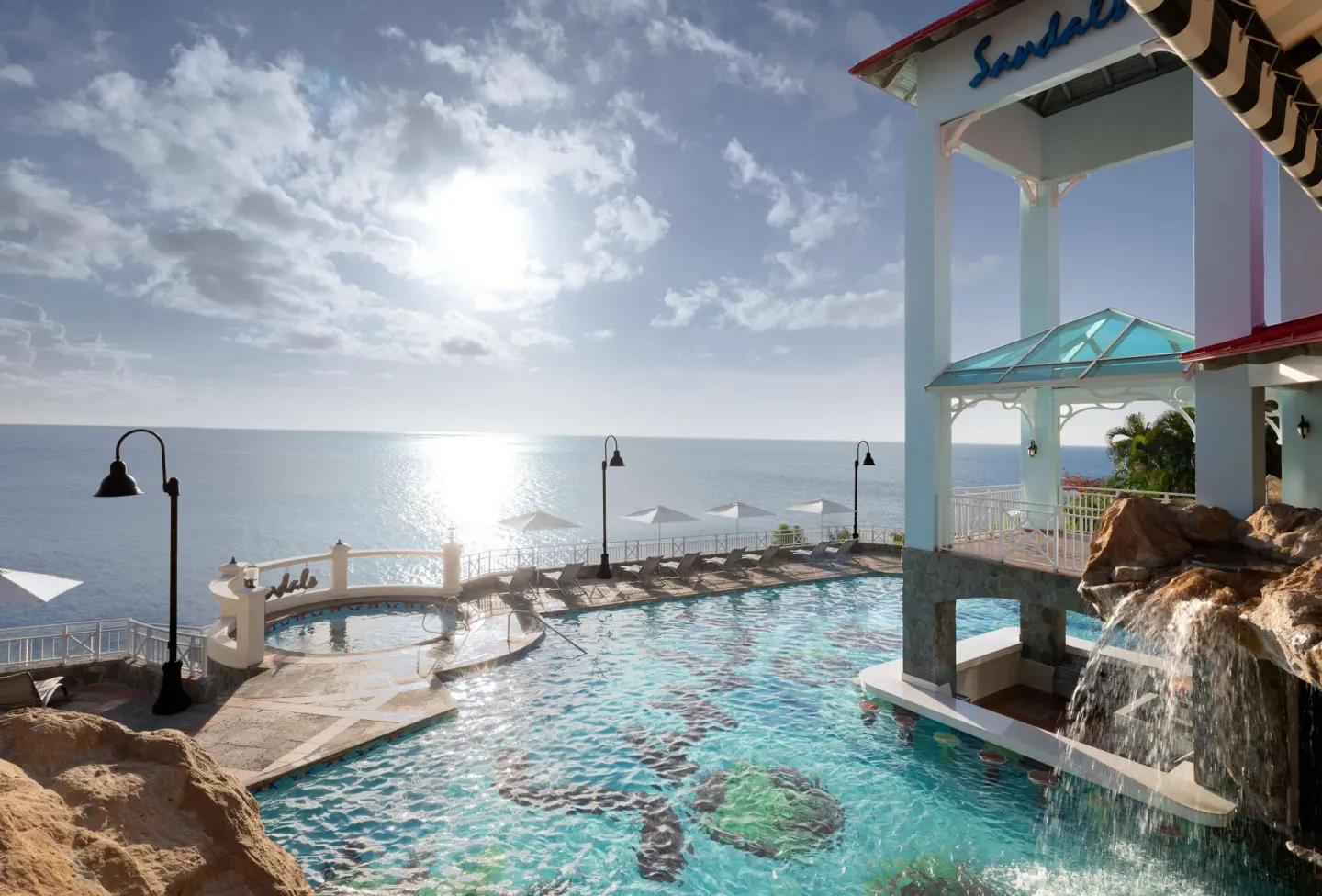 Sunlit oceanfront pool with waterfall and loungers at Sandals Regency La Toc.