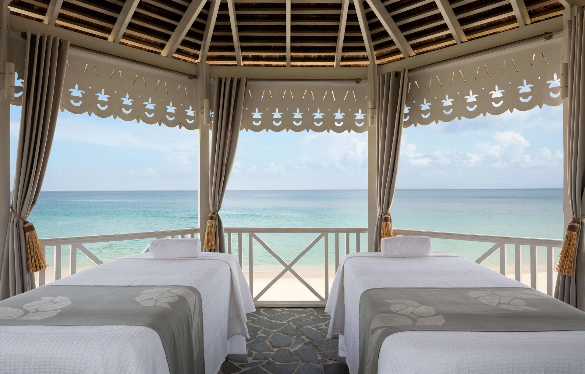 Two spa treatment beds face the beach and turquoise sea at Sandals Regency La Toc.