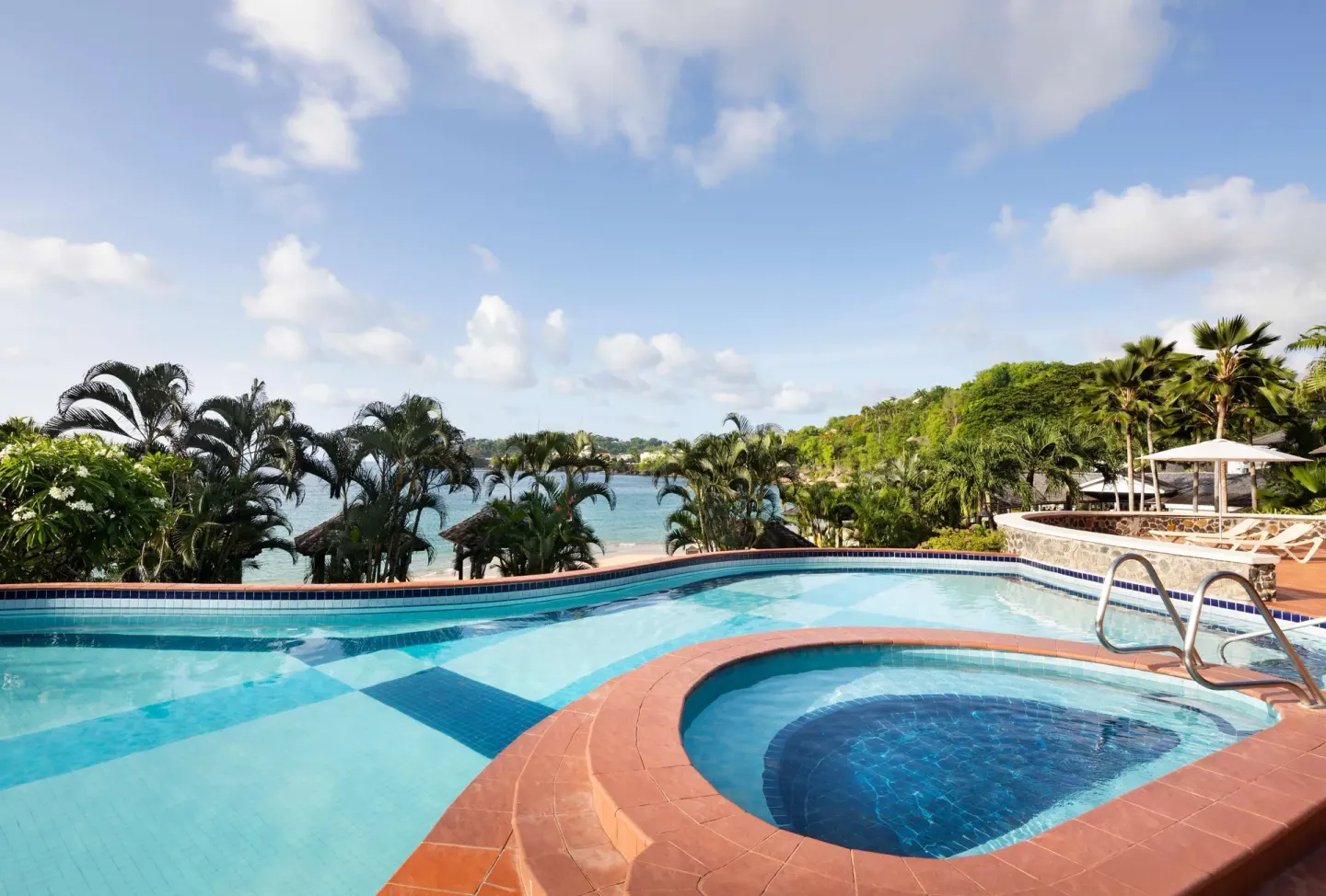 Swimming pool and round hot tub overlooking palms and the sea at Sandals Regency La Toc.