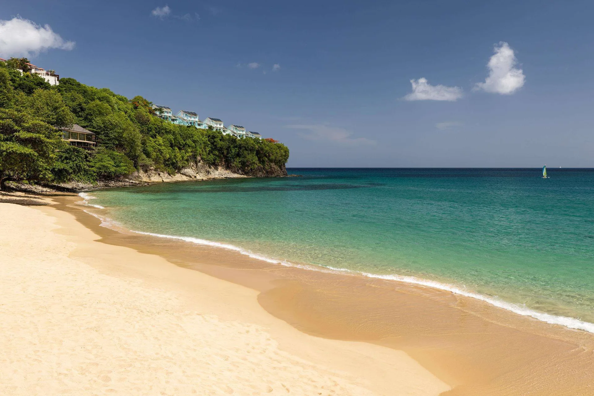 Sandy beach and calm turquoise water at Sandals Regency La Toc beneath a green headland.
