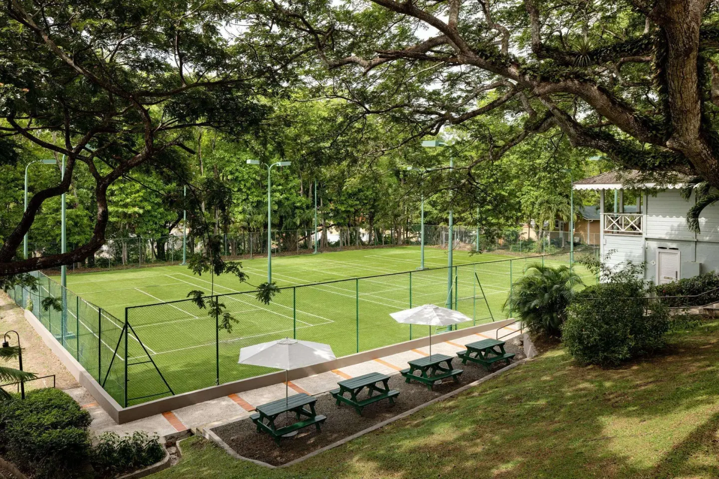 Tennis courts, benches and umbrellas sit under trees at Sandals Regency La Toc.
