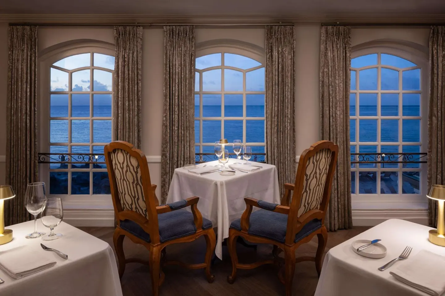 Elegant dining tables face arched ocean-view windows at Sandals Regency La Toc.