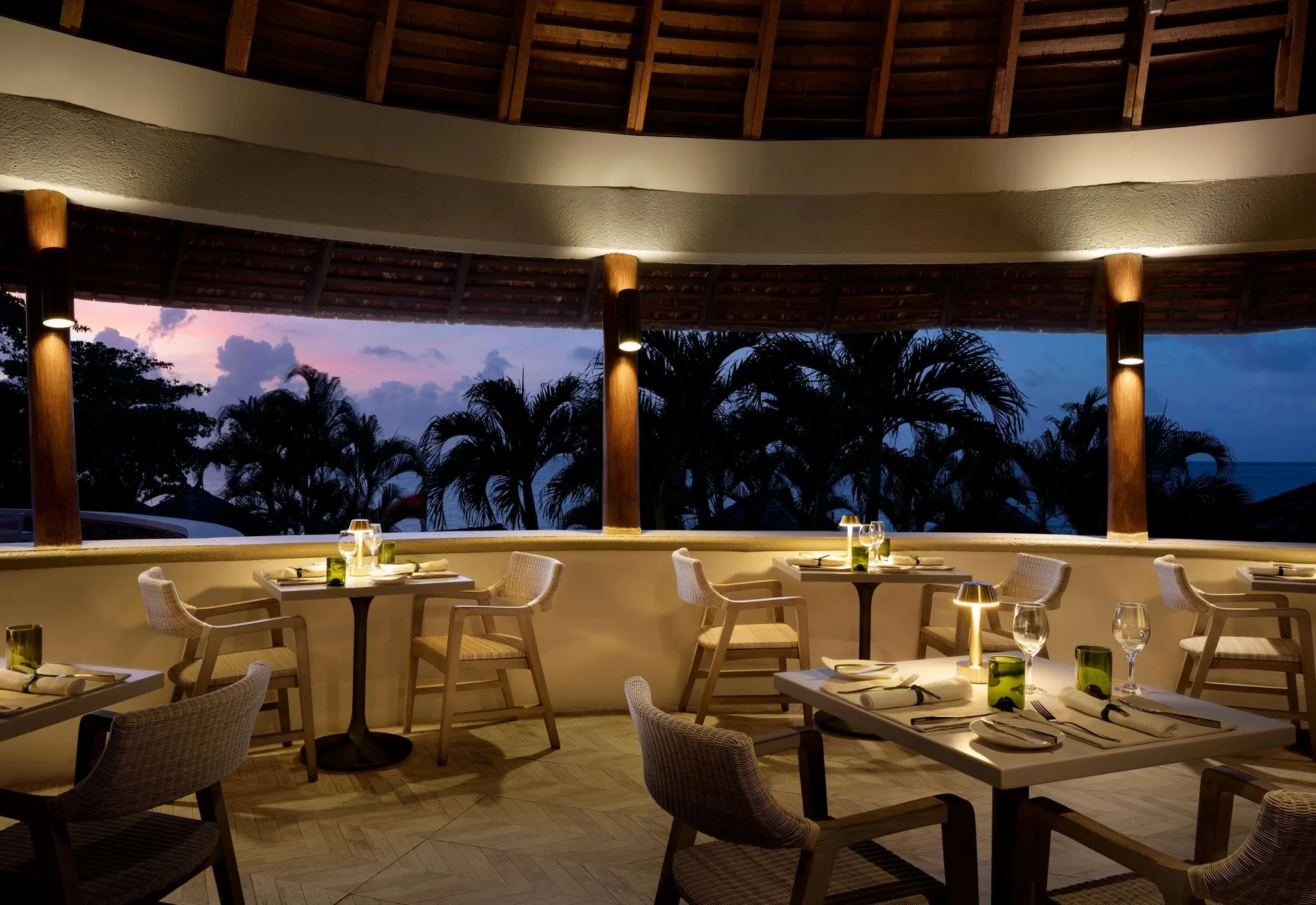 Open-air restaurant tables glow at dusk beside palm silhouettes at Sandals Regency La Toc.