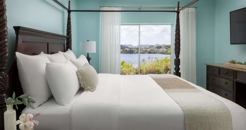 Four-poster king bed facing an ocean-view window at Sandals Regency La Toc.
