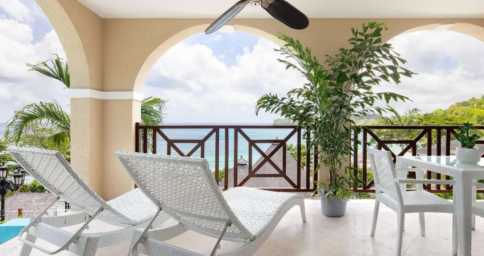 Covered ocean-view veranda with loungers and dining set at Sandals Regency La Toc.