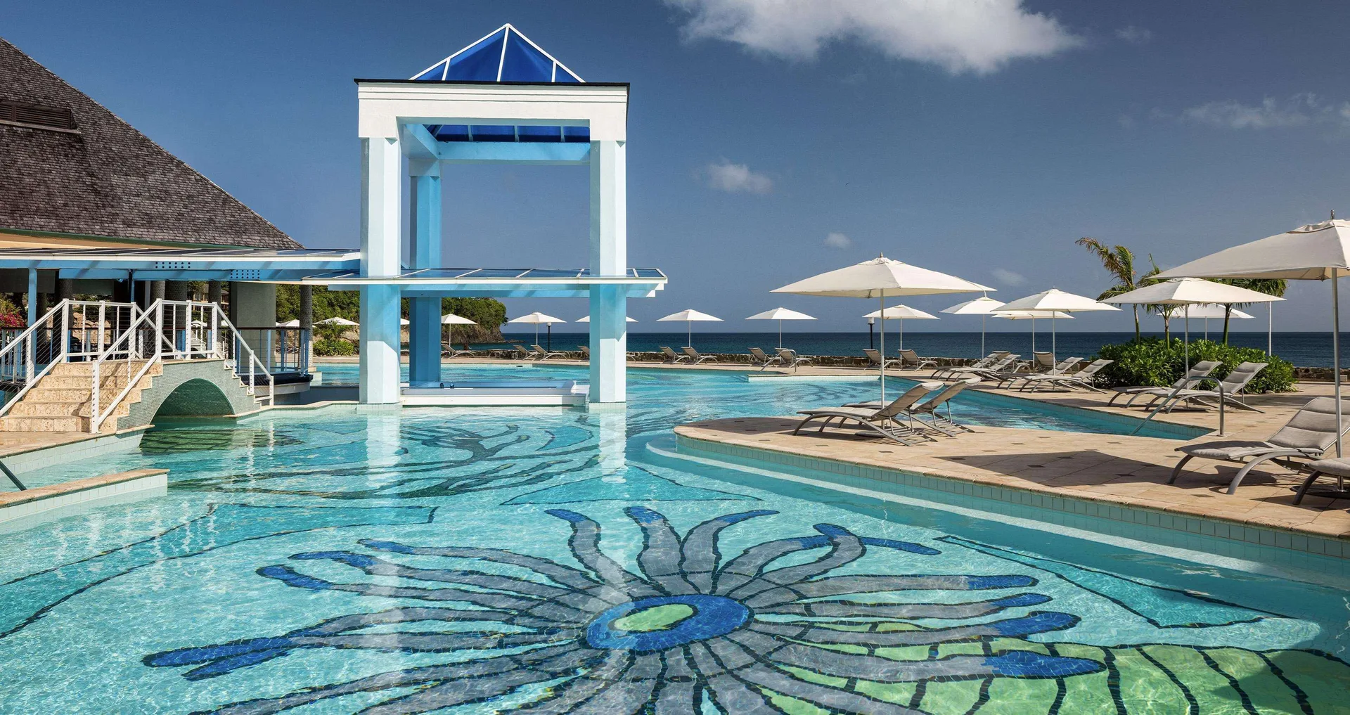 Pool with oceanfront loungers and umbrellas at Sandals Regency La Toc.