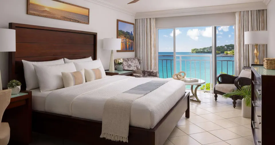 King bed and ocean-view balcony in an Emerald Oceanfront room at Sandals Regency La Toc.