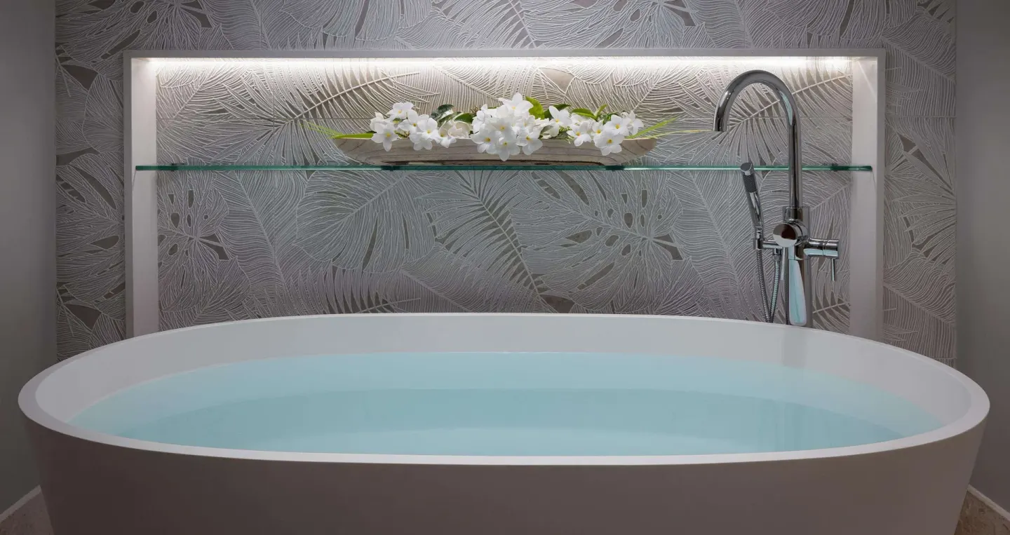 Freestanding soaking tub with floral wall detail in a villa bathroom at Sandals Regency La Toc.