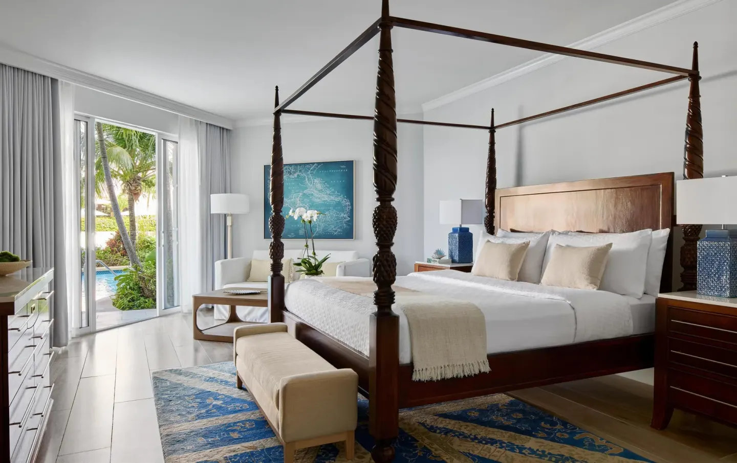 Four-poster king bedroom with patio doors and poolside greenery at Sandals Royal Bahamian.