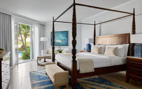Four-poster king bedroom with patio doors and poolside greenery at Sandals Royal Bahamian.
