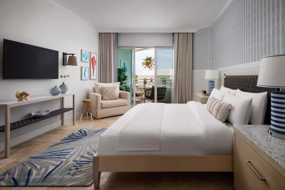Guest room at Sandals Royal Bahamian with a king bed, TV, armchair, and balcony doors.