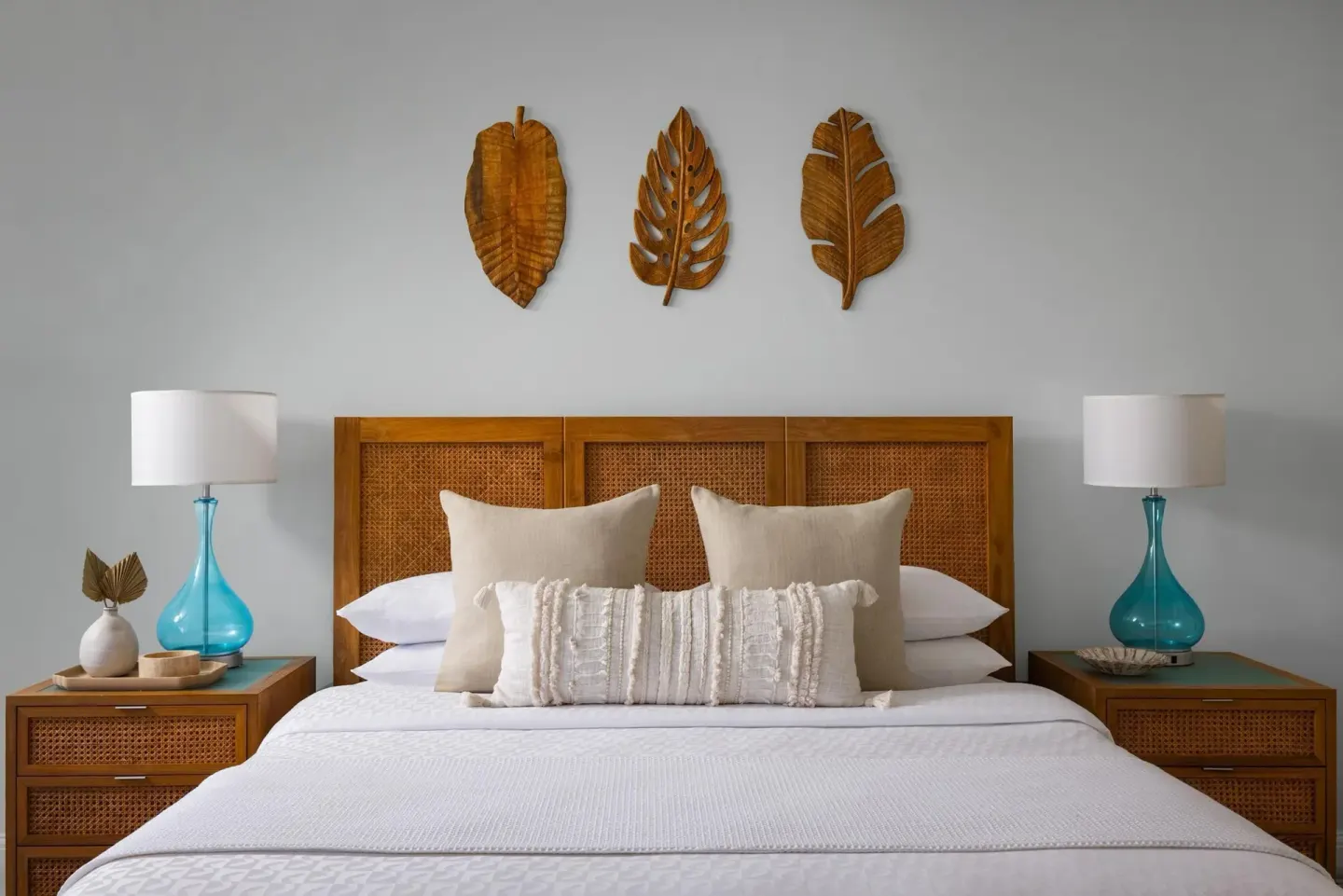 A king bed with cane headboard and turquoise lamps in a guest room at Sandals Royal Bahamian.
