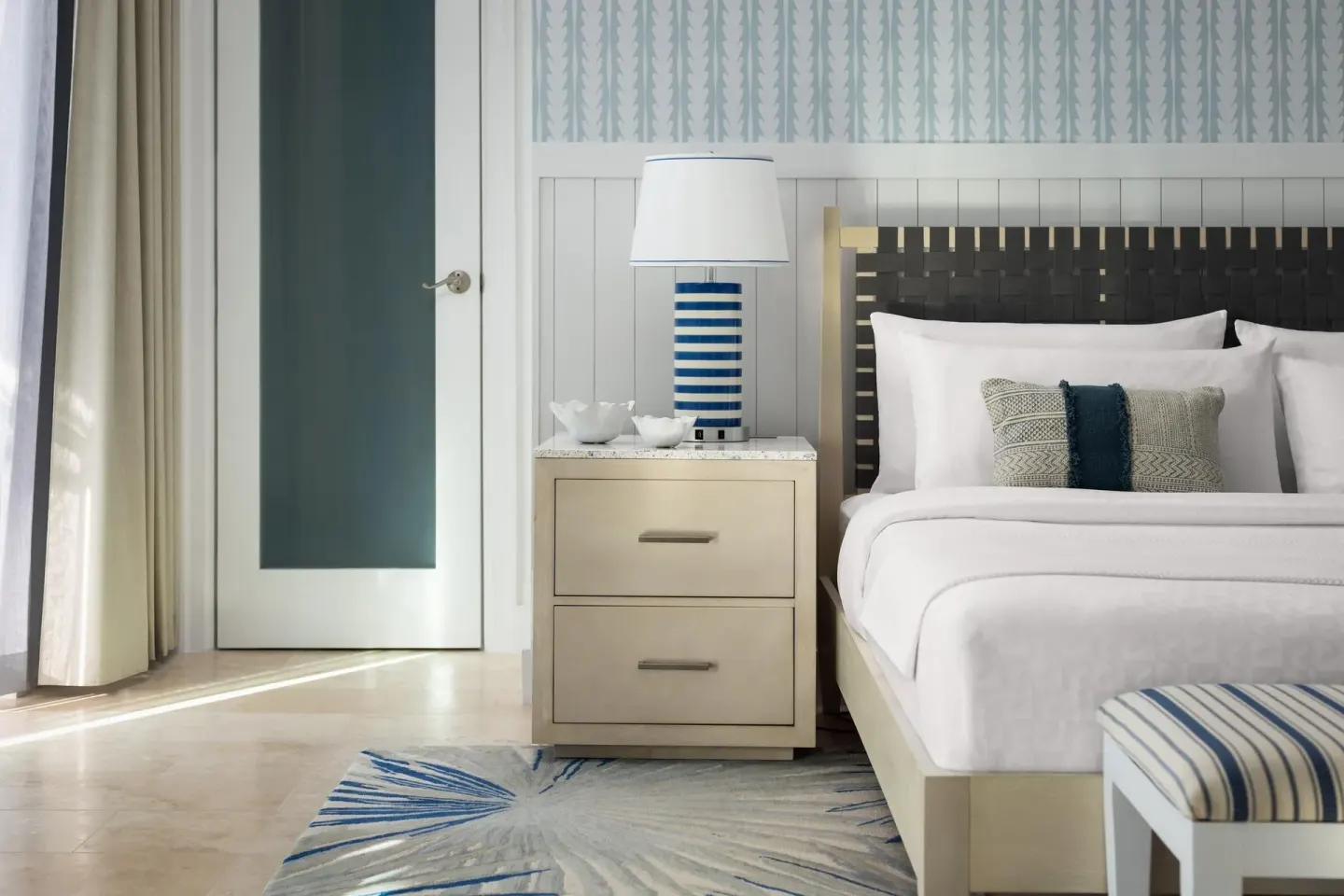 Guest room king bed with striped lamp and coastal decor at Sandals Royal Bahamian.